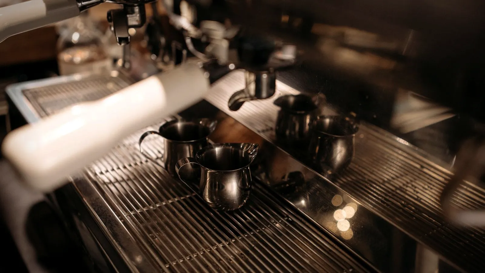 Small stainless steel milk pitchers on the drip tray of a commercial espresso machine