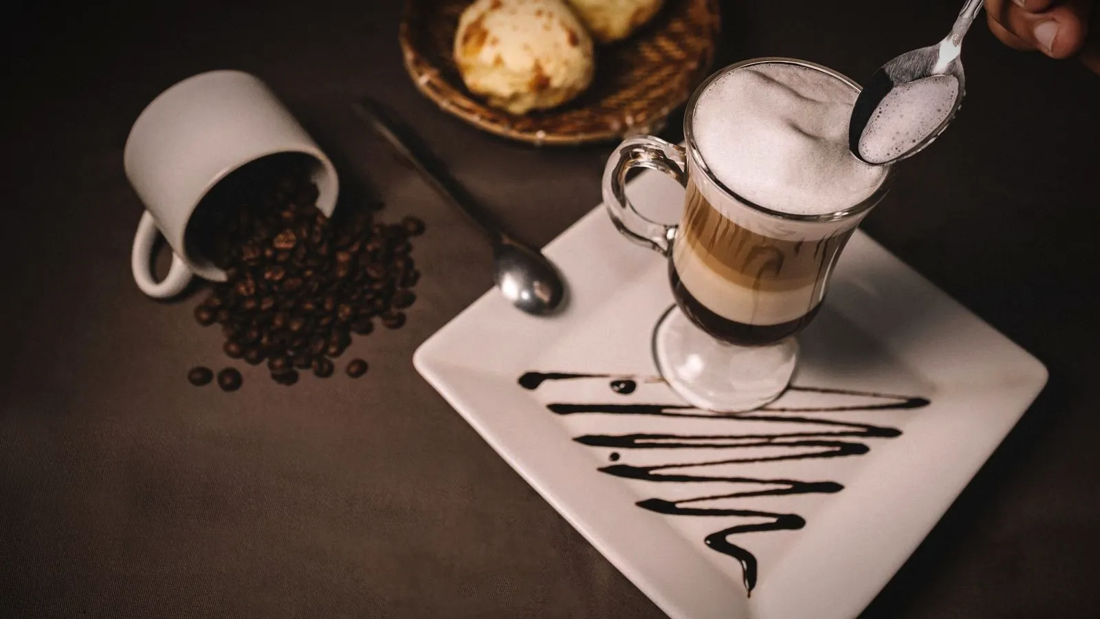 Spoon lifting thick milk foam from the top of a layered coffee in a glass