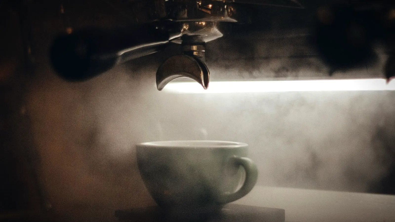 Steam drifting around a cup under an espresso machine group head