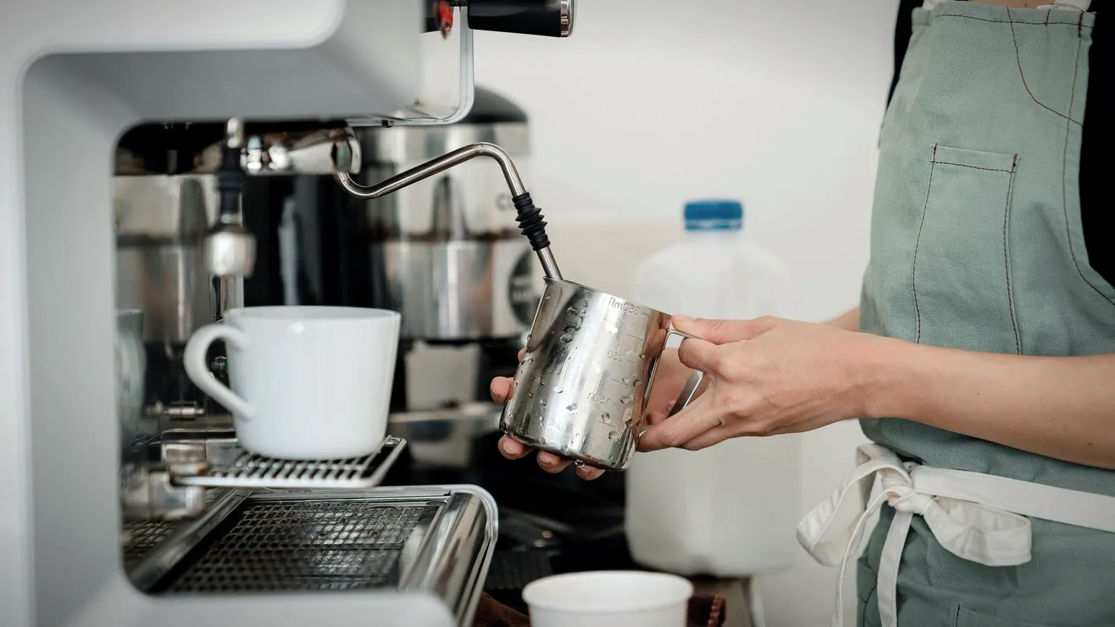Barista steaming milk in a stainless steel pitcher with the steam wand of an espresso machine