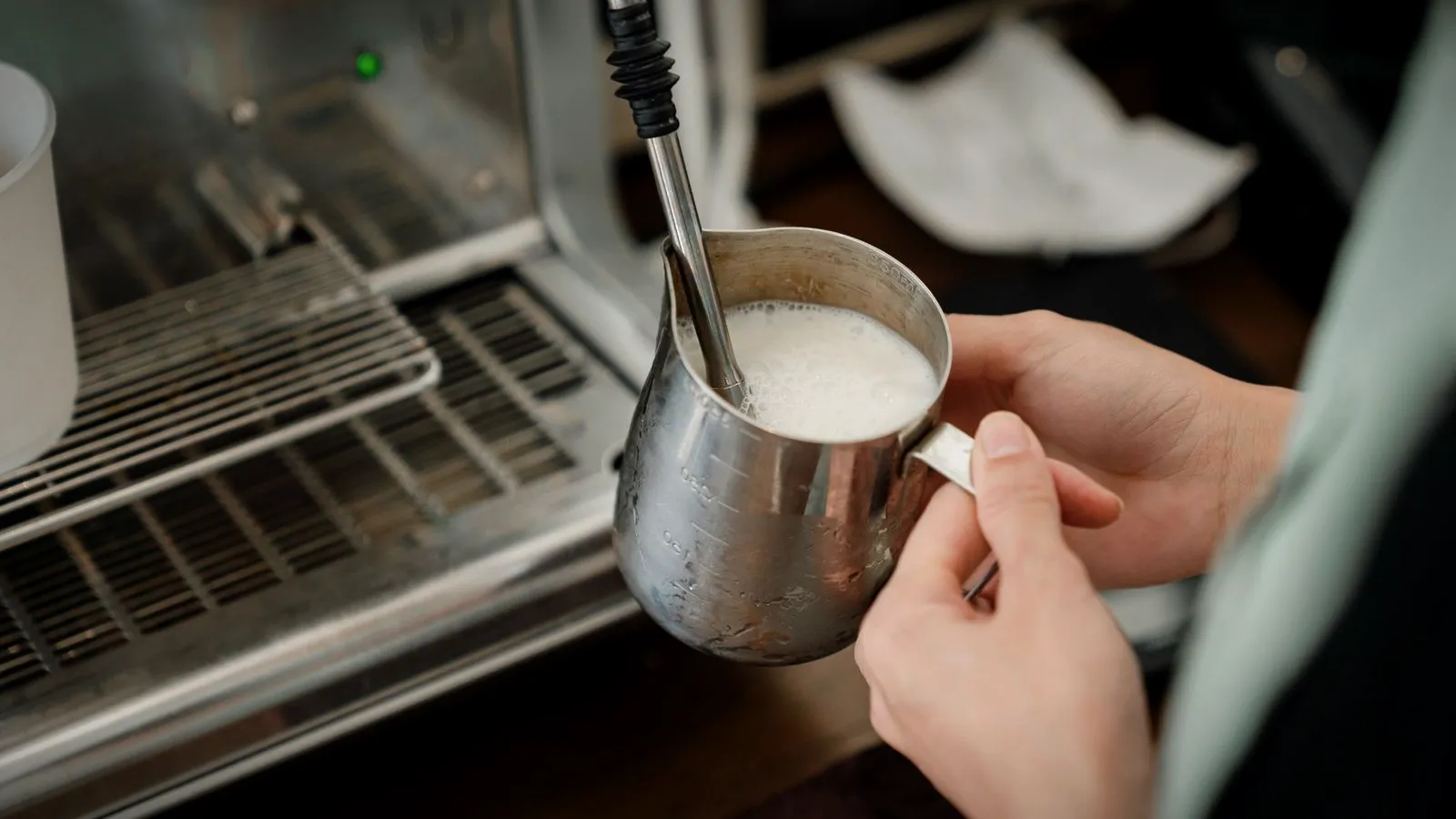 Milk being steamed in a stainless steel pitcher with an espresso machine steam wand