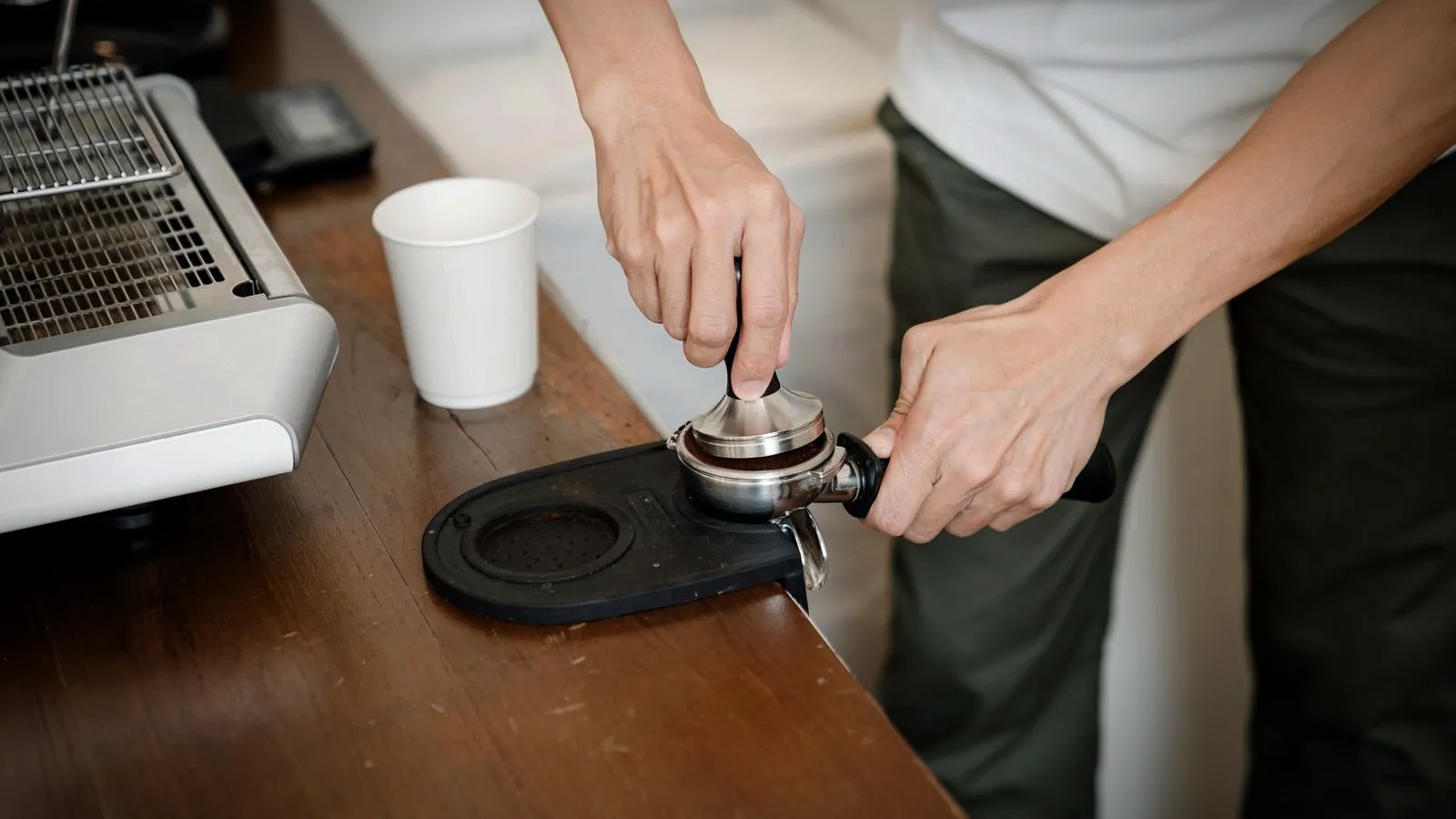 A home barista tamping ground coffee in a portafilter on a rubber mat