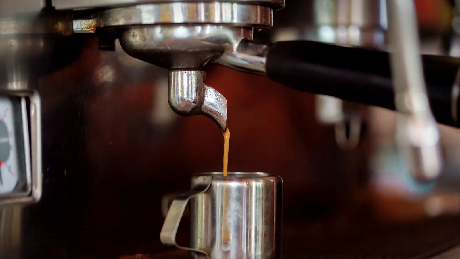 Thin stream of espresso running from a portafilter spout into a small steel pitcher