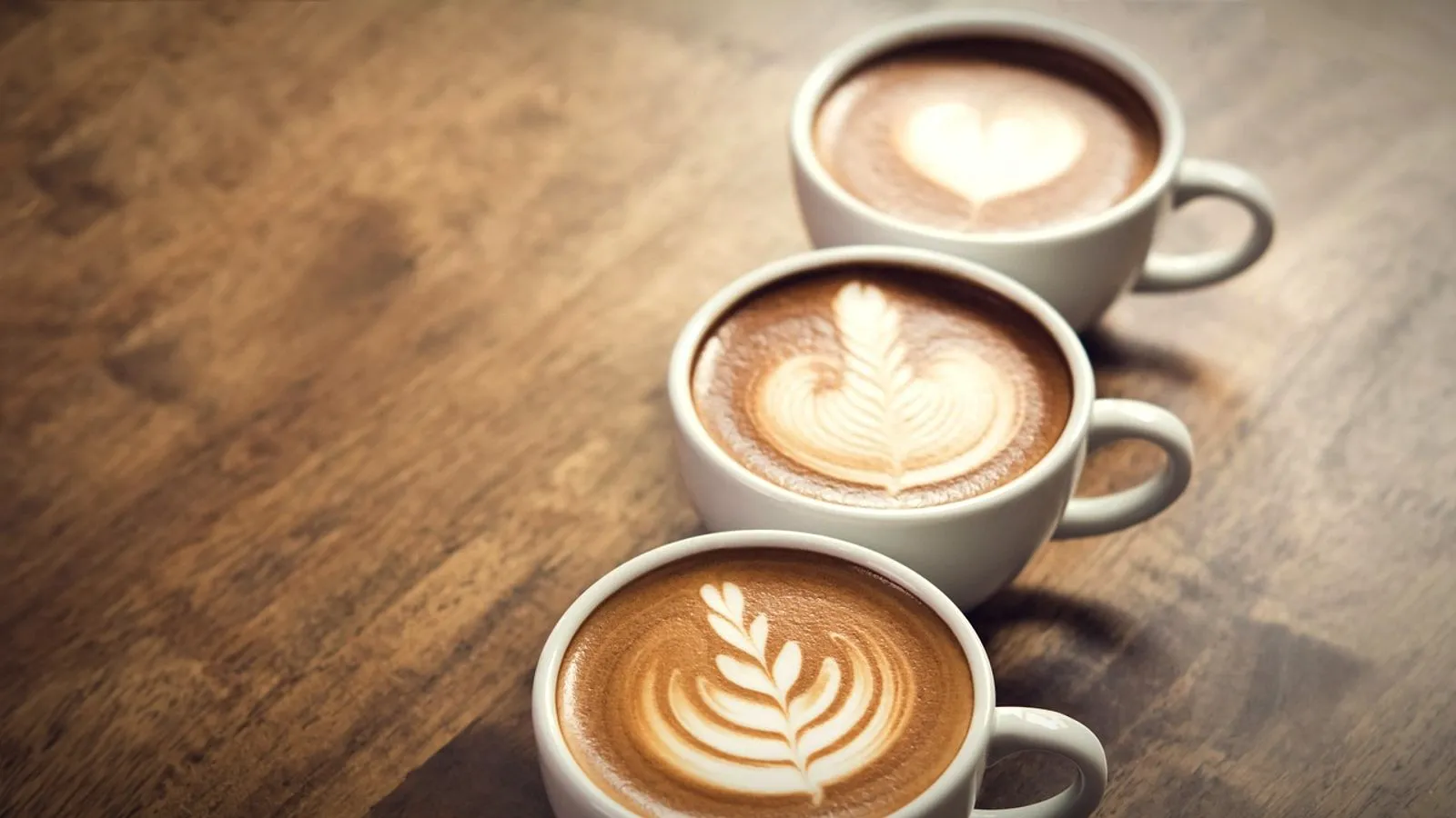 Three cups of milk-based espresso drinks with latte art on a wooden table