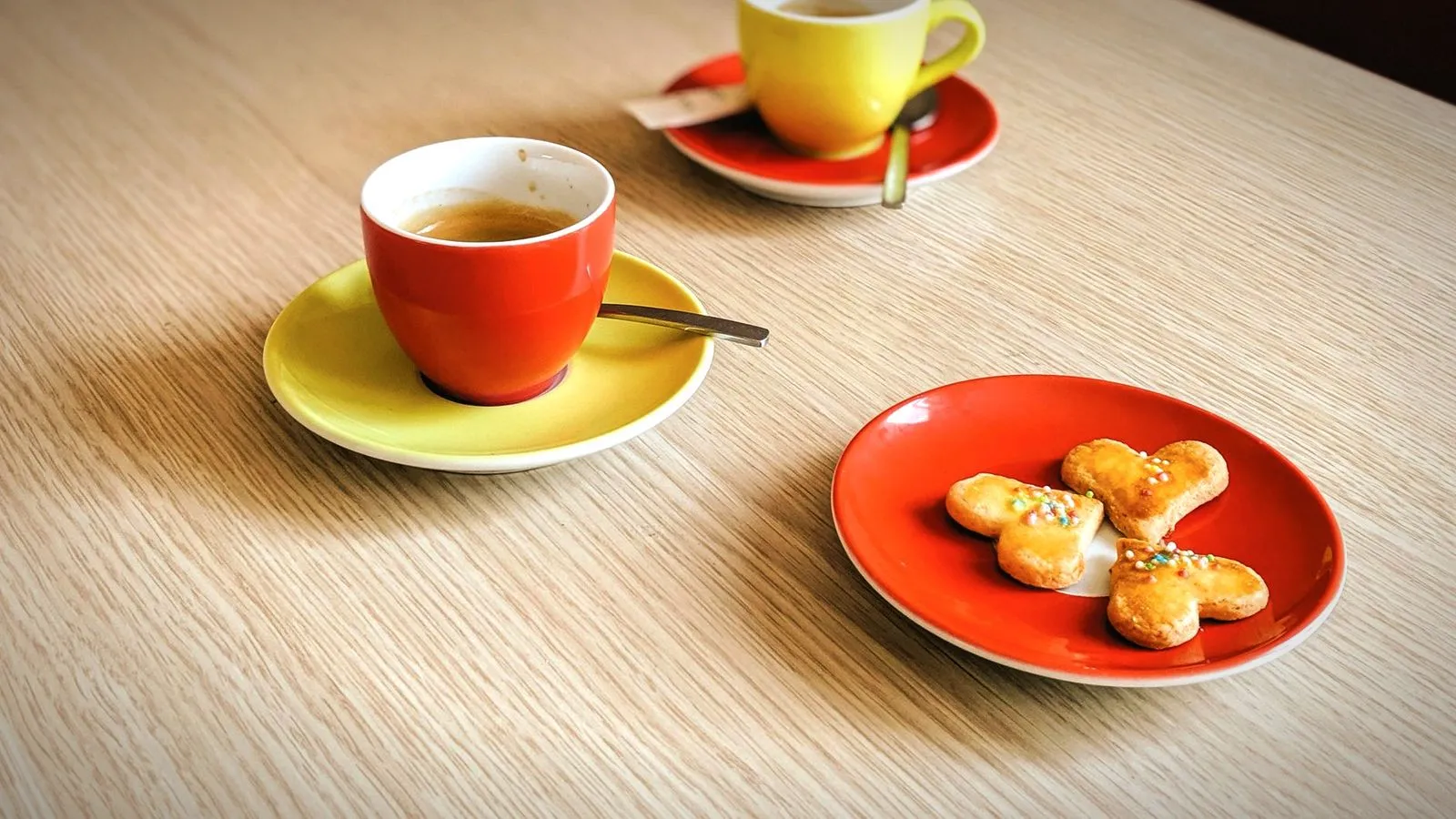 Two espresso cups on colorful saucers with cookies on a light wooden table