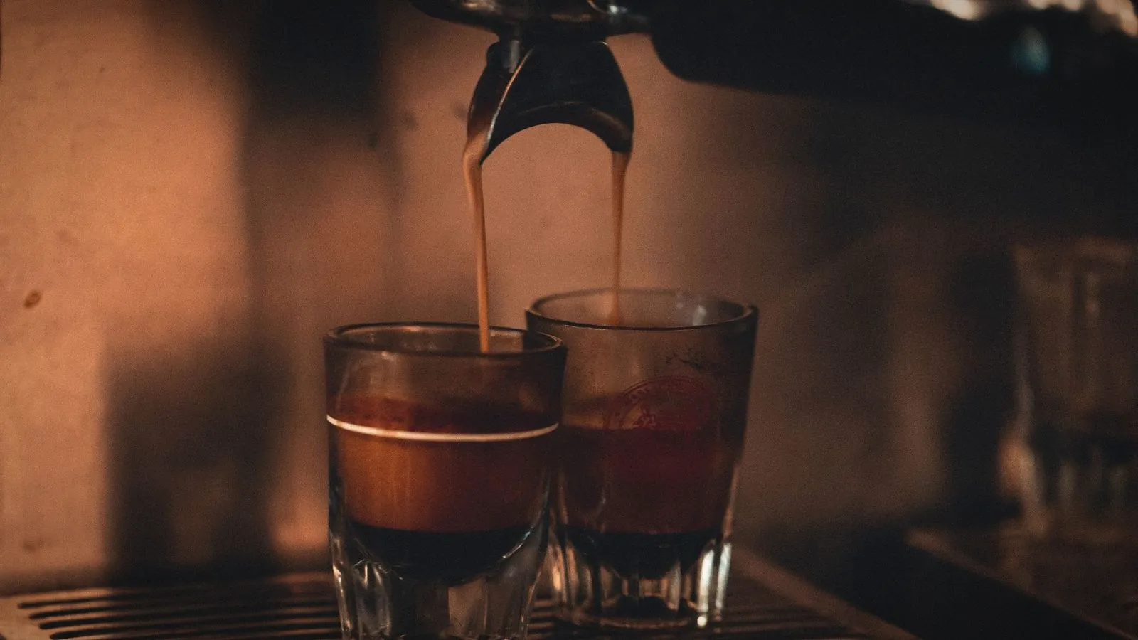 Espresso pouring from a double spout into two small shot glasses on a machine’s drip tray