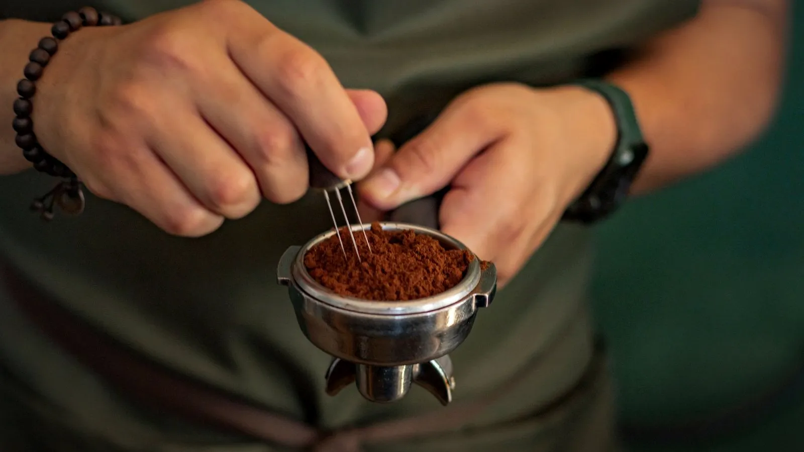 Barista stirring fresh espresso grounds in a portafilter with a fine needle WDT tool