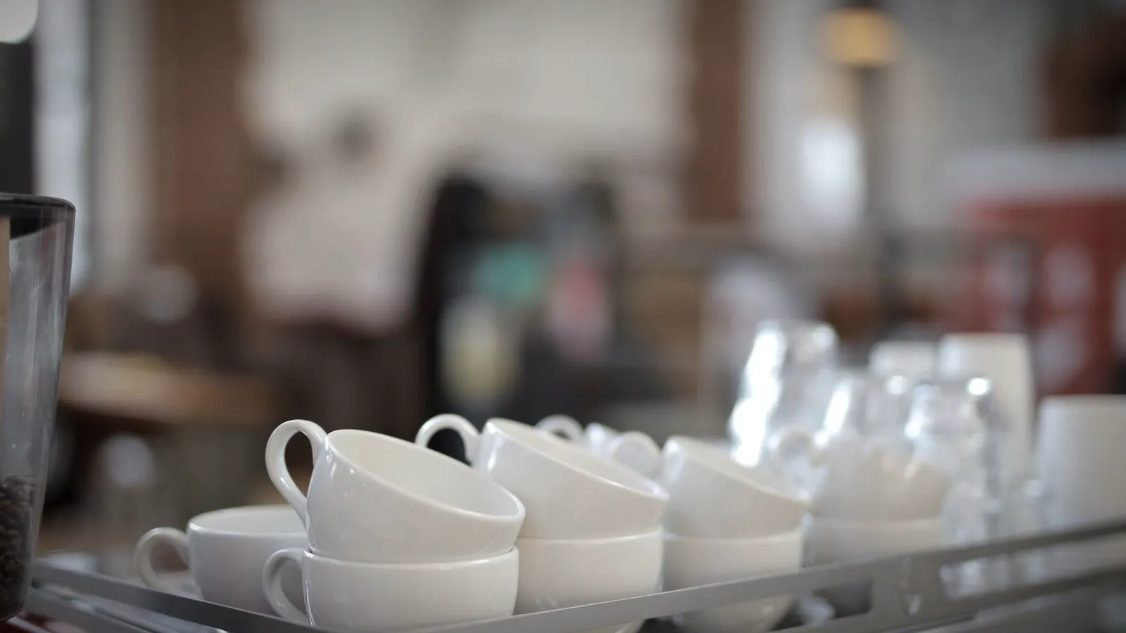 Stacked white cups warming on the cup tray on top of an espresso machine