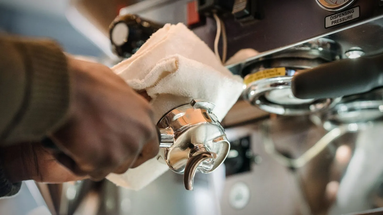 Barista wiping a portafilter basket clean with a cloth next to the group head of an espresso machine